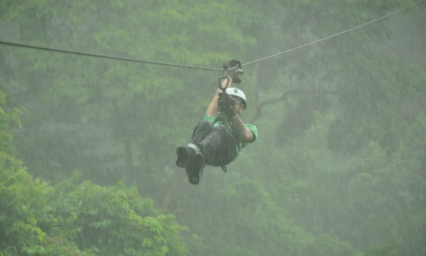 Thrill-seeker ziplining through Monteverde Cloud Forest canopy with Arenal Volcano visible in distance - Macaws Adventure Tours by Pablo C